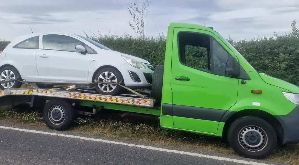 Az Recovery's lime-green Mercedes Sprinter flatbed with a white Vauxhall Corsa strapped on, parked on a grass verge